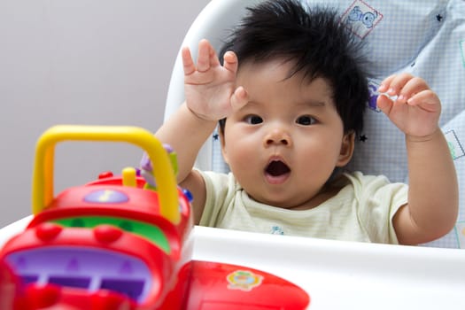 Little Asian baby girl on high chair playing with airplane toy