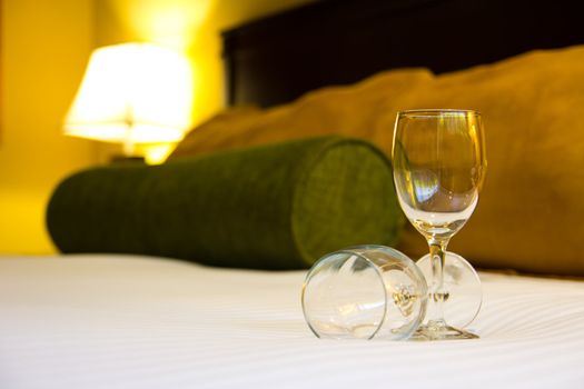 Two empty wine glasses on bed with yellow light illuminate at the back