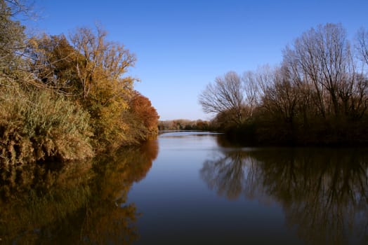 Landscape of a river on autumn, beautiful reflections and colors. Clean blue sky
