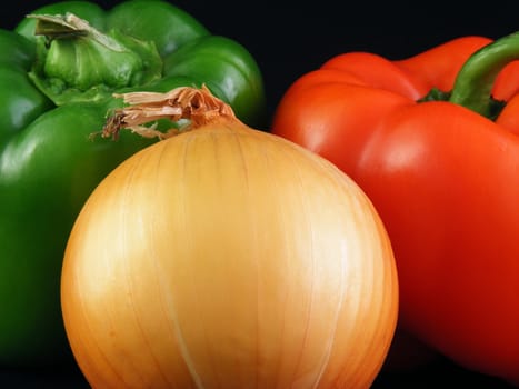 A yellow onion, a green bell pepper and a red bell pepper against a black background.