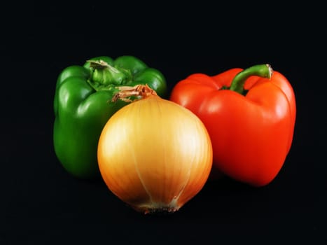 A yellow onion, a green bell pepper and a red bell pepper against a black background.