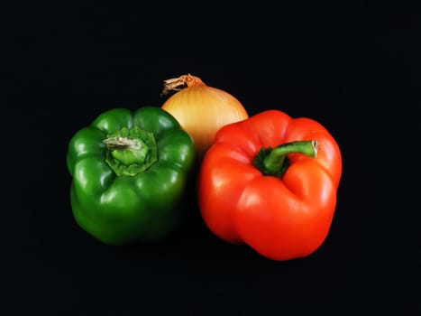 A yellow onion, a green bell pepper and a red bell pepper against a black background.