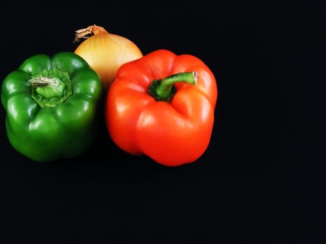 A yellow onion, a green bell pepper and a red bell pepper against a black background.