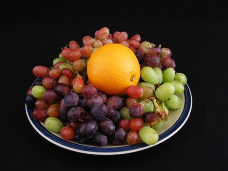 An orange nestled in a bed of grapes.