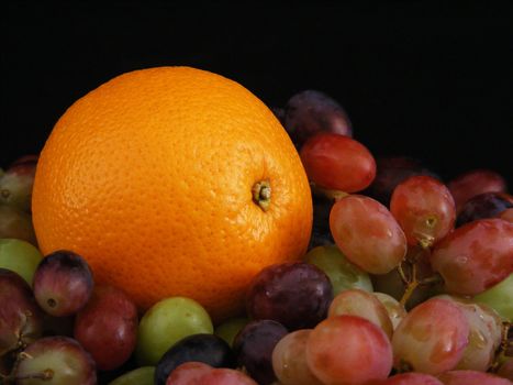 An orange nestled in a bed of grapes.