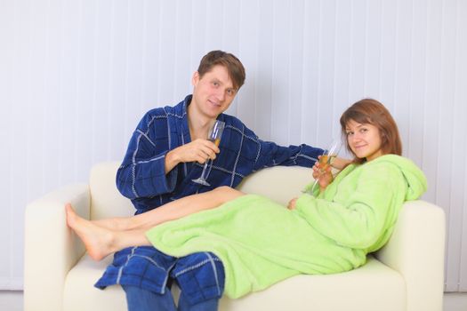 The young couple drinks sparkling wine on a sofa in dressing gowns