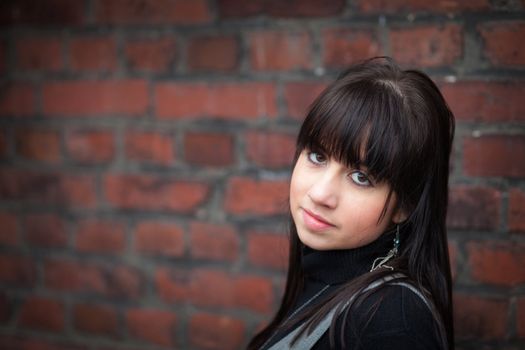Pensive brunette girl against a red brick wall; blurred background