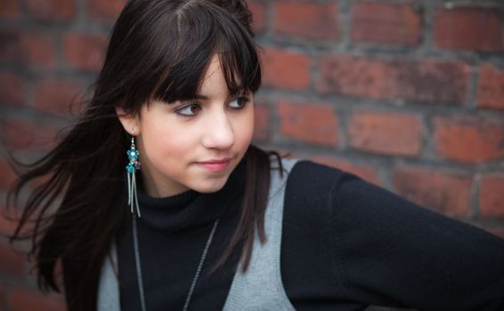 Pensive brunette girl against a red brick wall; blurred background