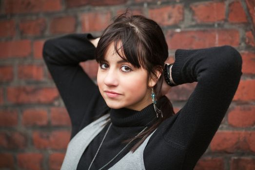 Young brunette woman outdoors, her hands are on her nape; selective focus (blurred background)