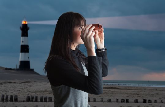 Brunette woman looking via binoculars; lighthouse on background