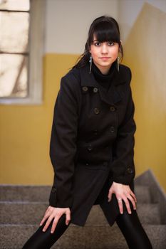 pretty brunette girl in a black coat standing on stairs