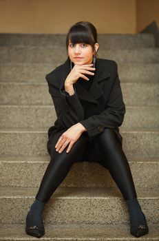 pretty brunette girl dressed in black clothes sitting on stair step