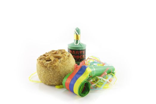 Small tasty pork pie with party blower and party popper with streamers on a reflective white background
