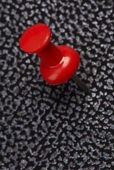 Red thumbtack on a notebook from an artificial leather. A close up