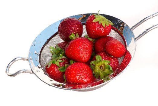 Ripe strawberry in a colander under a jet of pure water.