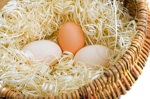 Three fresh eggs in a basket with a straw.