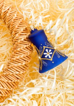 Blue christmas bell and part of straw decoration on yellow stripes