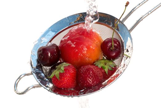 Ripe strawberry, cherry and peach in a colander under a jet of pure water.