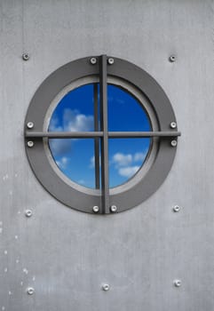 Silver metal door with porthole window with view on sky