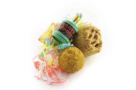Small tasty pork pie, small round scotch egg and streamers with party popper on a reflective white background