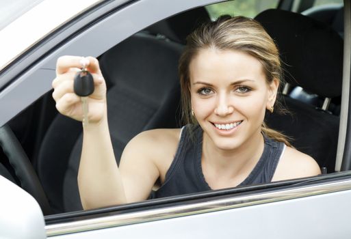 Beautiful young happy woman in car showing the keys