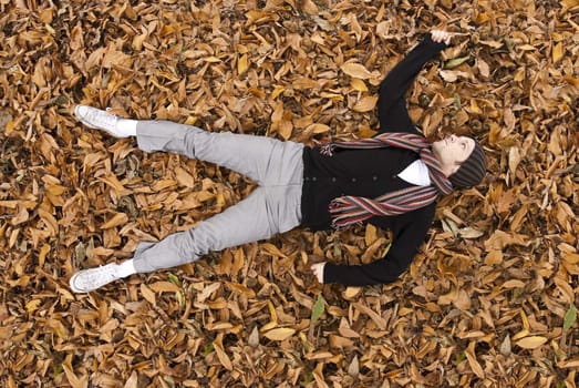 High angle full body shot of young man laying on the yellow leaves covered ground.