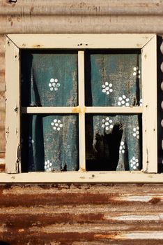 an old forlorn window with ripped and worn curtain in the wall of an iron house