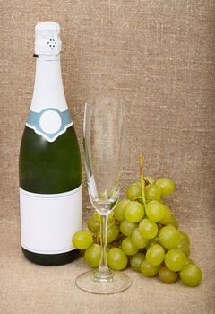 Still-life from a bottle of a sparkling wine, empty glass and grapes against a canvas