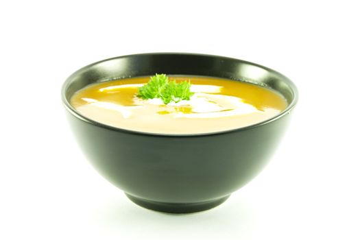 Rich red deliicious tomato soup in a small round black bowl with cream and a sprig of parsley on a white background