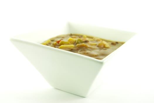 Hot chunky vegetable soup in a small square white bowl on a white background