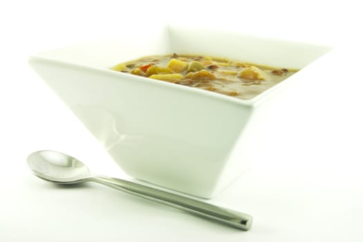 Hot chunky vegetable soup in a small square white bowl with a small spoon on a white background