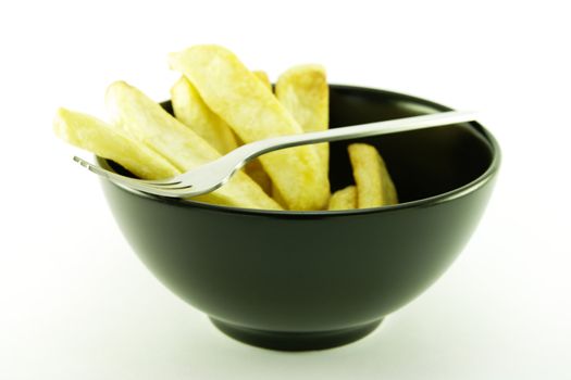 Golden cooked frys in a small black bowl with a small fork on a white background