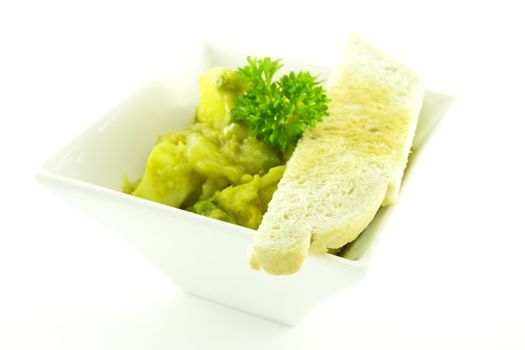 Spicy hot curry in a small square white bowl with a sprig of parsley and toast on a white background