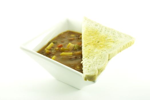 Hot chunky vegetable soup in a small square white bowl with toast on a white background