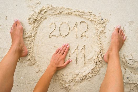 Female hand erasing numbers 2011 on the sand