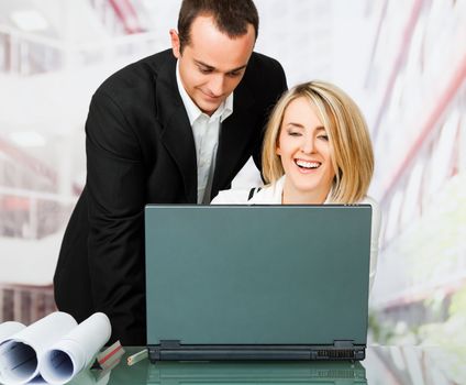 Male and female architects smiling behind laptop
