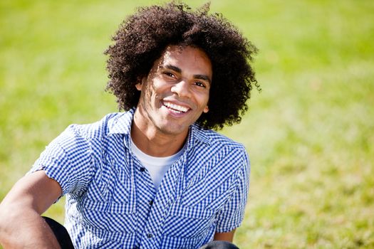 A young African American male sitting on the grass