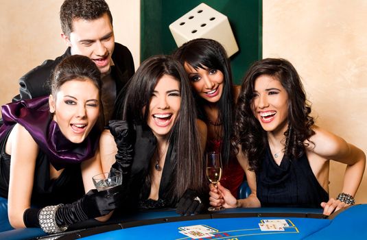 Young happy people sitting in casino behind black jack table, having fun
