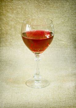 One glass with red wine against a brown drapery