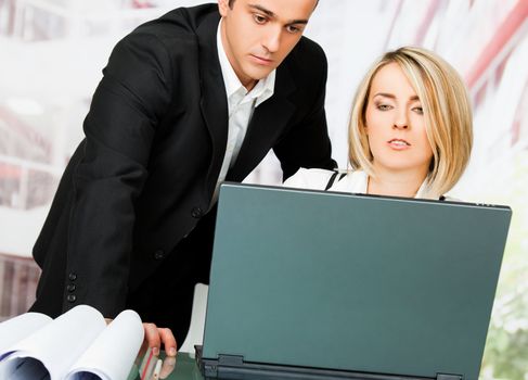 Male and female architects behind laptop and blueprints, looking serious