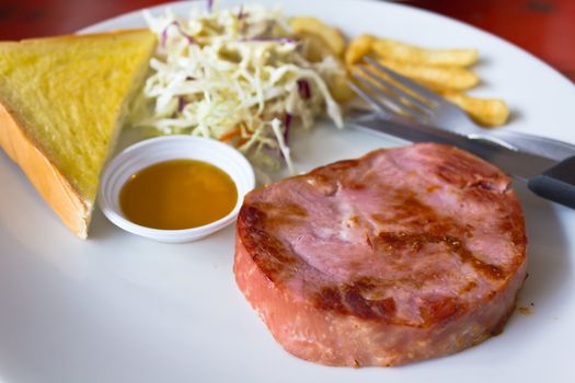 Ham steak with bread on a white dish