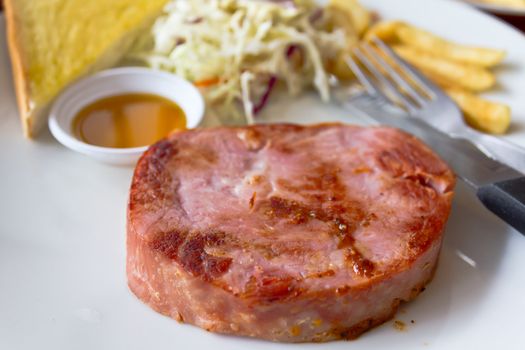 Ham steak with bread on a white dish