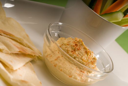 middle eastern hummus dip on a glass bowl with homemade pita bread and raw vegetable