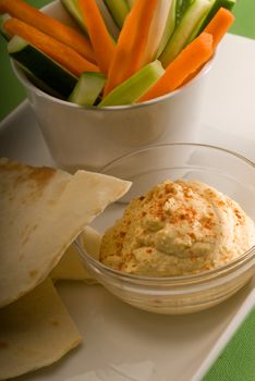 middle eastern hummus dip on a glass bowl with homemade pita bread and raw vegetable