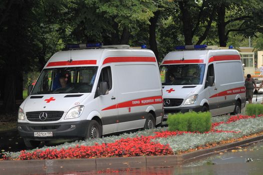 ambulances are parked in the park against the backdrop of flower beds and trees