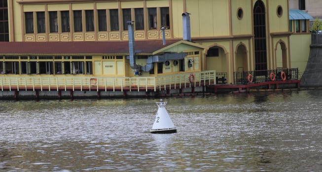 buoy on the river on a gray background waves. In the background, building on the banks of yellow with a brown roof