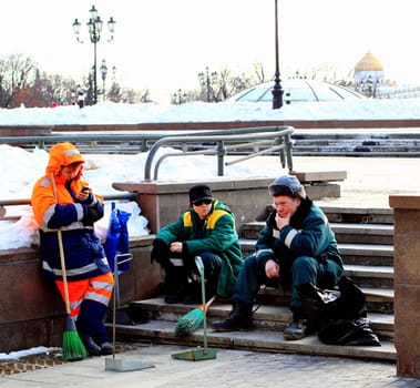 Three people - janitors relax after work on the steps on the background of the urban landscape