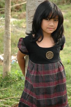 little asian girl stand up beside the tree in park