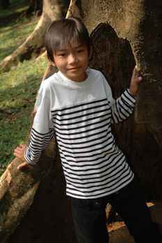 little asian boy stand up beside the tree in park