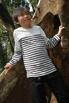 little asian boy stand up beside the tree in park